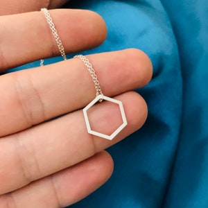 May include: A silver necklace with a hexagonal pendant. The pendant is a simple geometric shape with a hollow center.