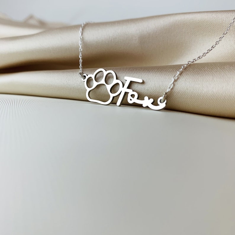 May include: Silver necklace with a paw print charm and the name "Fox" written in cursive.