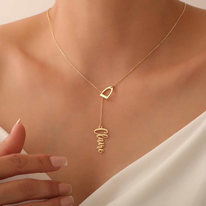May include: Gold necklace featuring a horseshoe pendant and a dangling nameplate inscribed with the name "Claire".