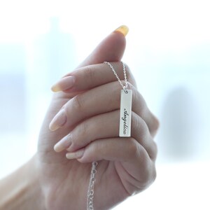 Puede incluir: Un collar de plata con un colgante rectangular que dice "angelica" en escritura cursiva.