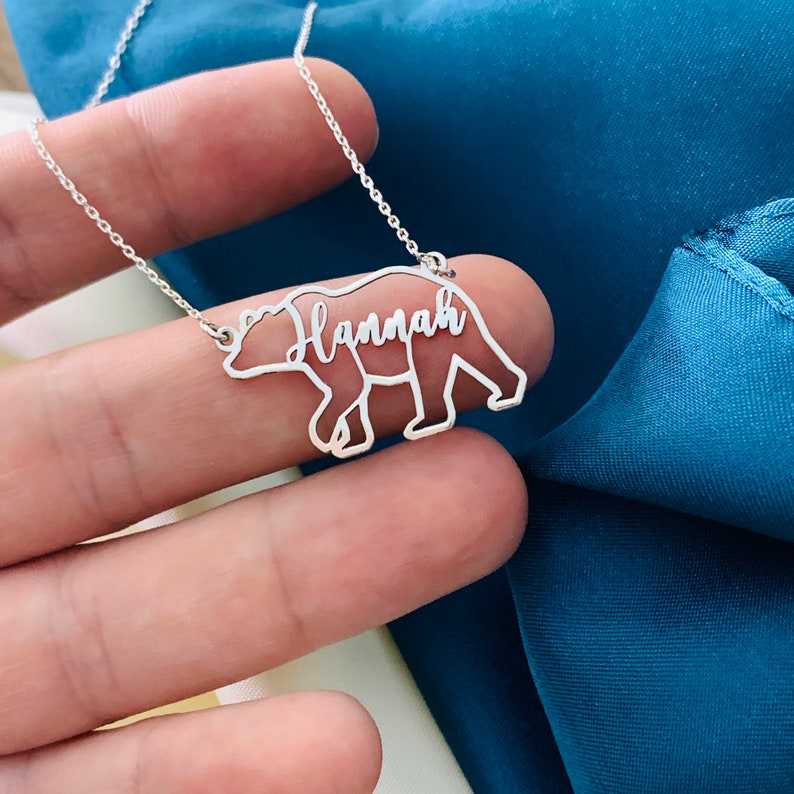 Peut inclure: Un collier en argent avec un pendentif en forme d'ours. Le contour de l'ours est rempli du nom "Hannah" en &eacute;criture cursive.