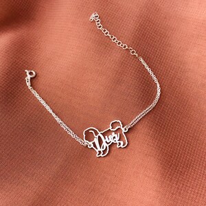 May include: Silver chain bracelet featuring a delicate, cutout design of a dog with the word "Dues" written inside the silhouette.