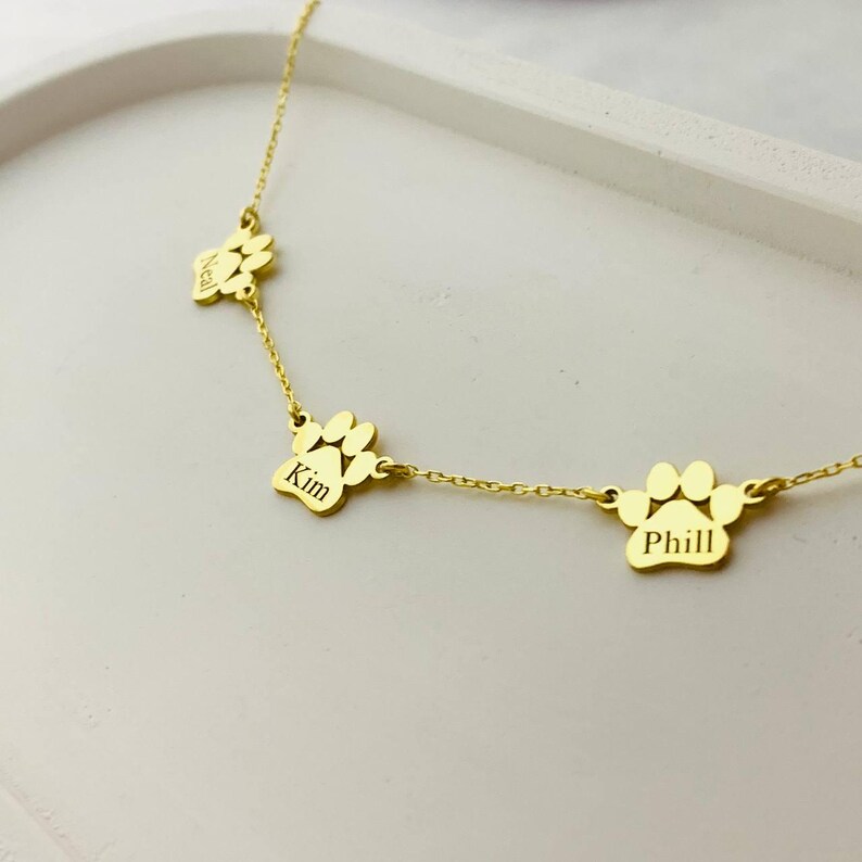 May include: Gold necklace with three paw print charms, each engraved with a name: Neal, Kim, and Phill.