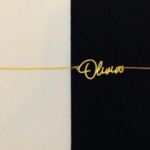 K&ouml;nnte beinhalten: Eine goldene Halskette mit dem Namen "Olivia" in Schreibschrift.