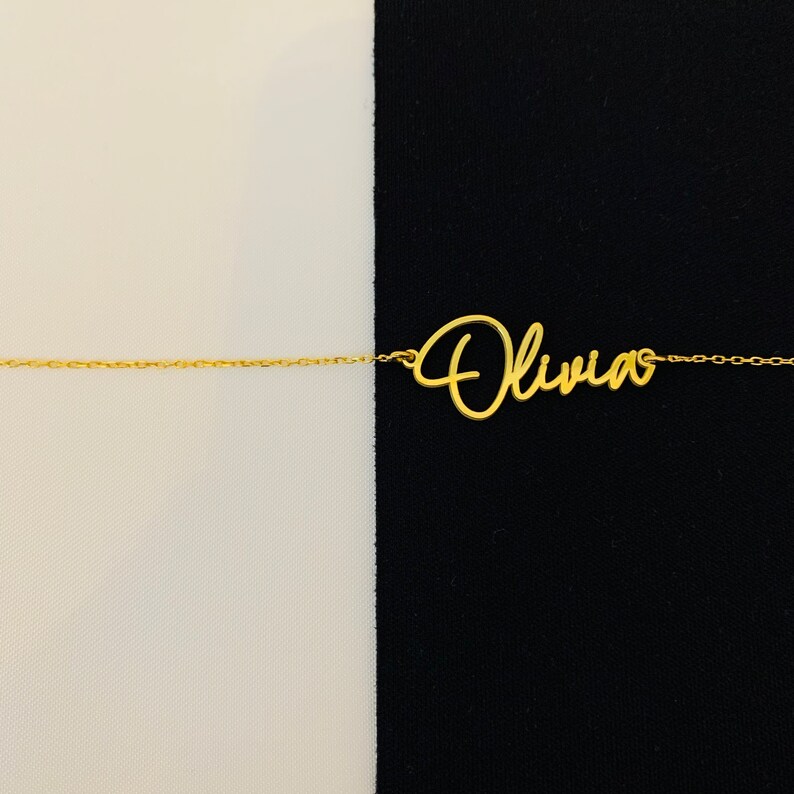 K&ouml;nnte beinhalten: Eine goldene Halskette mit dem Namen "Olivia" in Schreibschrift.