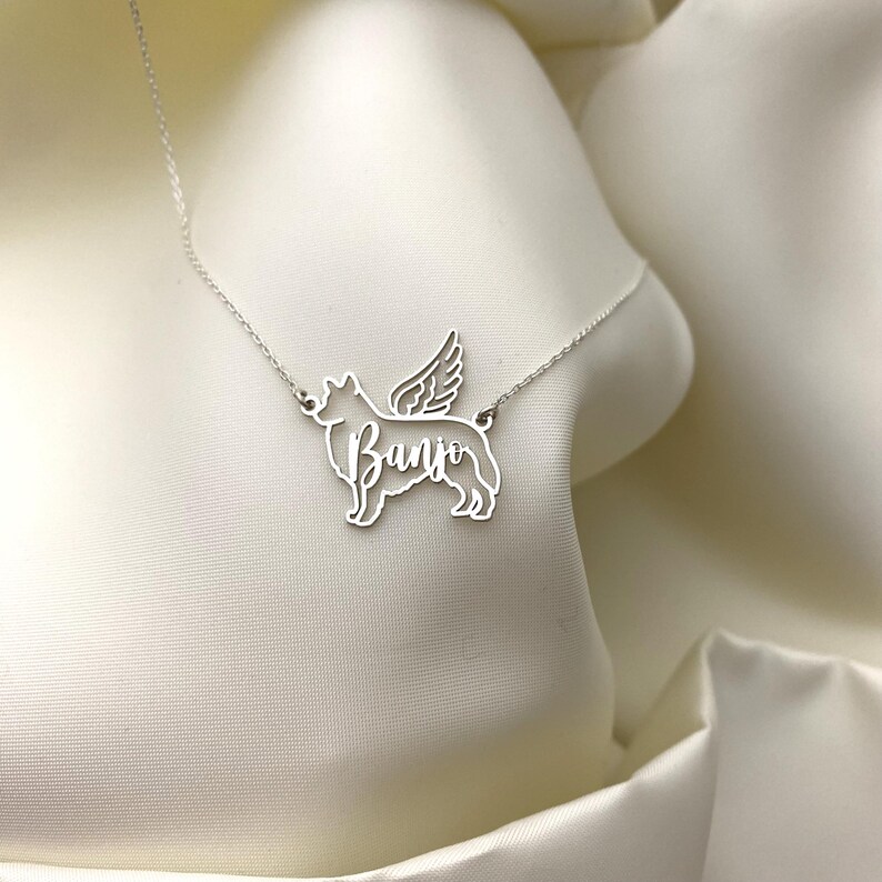May include: Silver necklace with a dog silhouette pendant. The dog has wings and the name "Banjo" is cut out of the pendant.