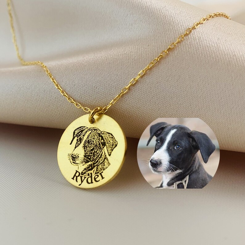 May include: A gold pendant necklace with a detailed engraved portrait of a dog. The round pendant has the dog's name, "Ryder," engraved below the image. A small photo of the dog is next to the pendant.