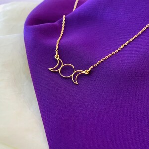 K&ouml;nnte beinhalten: Eine goldene Halskette mit einem dreifachen Mond-Anh&auml;nger. Der Anh&auml;nger ist ein schlichtes Design mit drei Mondsicheln.