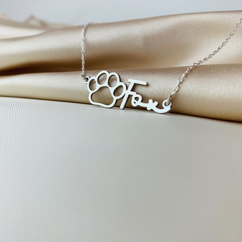 Peut inclure: Collier en argent avec un pendentif en forme de patte de chien et le nom "Fox" &eacute;crit en cursive.