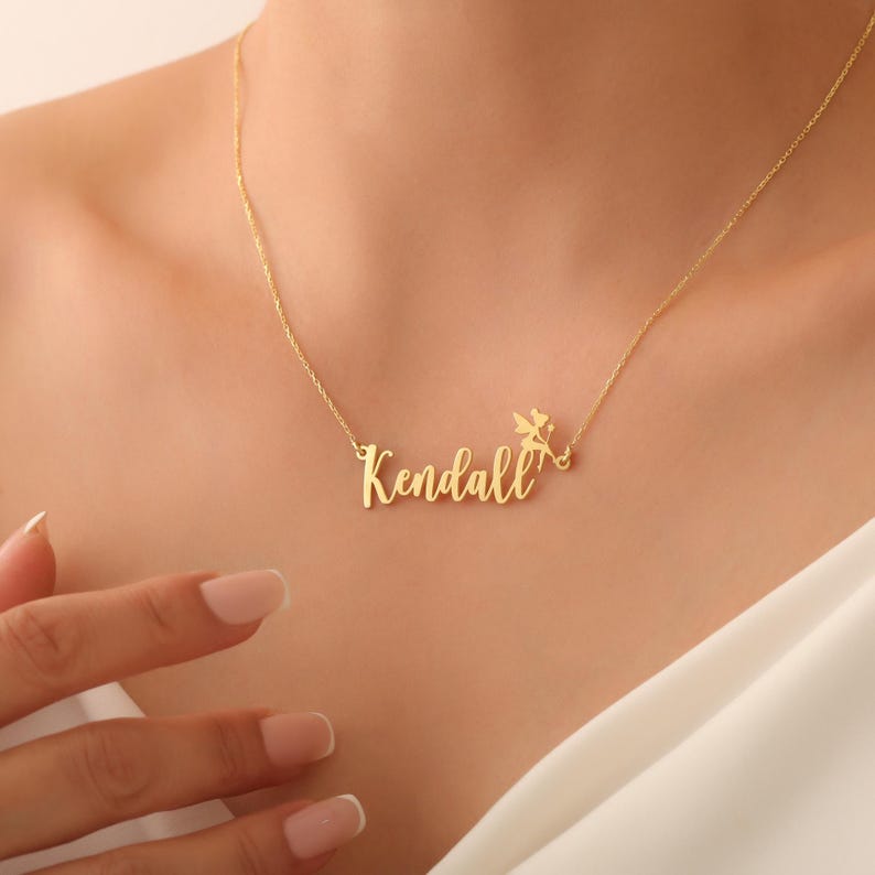 May include: Gold necklace with the name "Kendall" and a small angel charm.