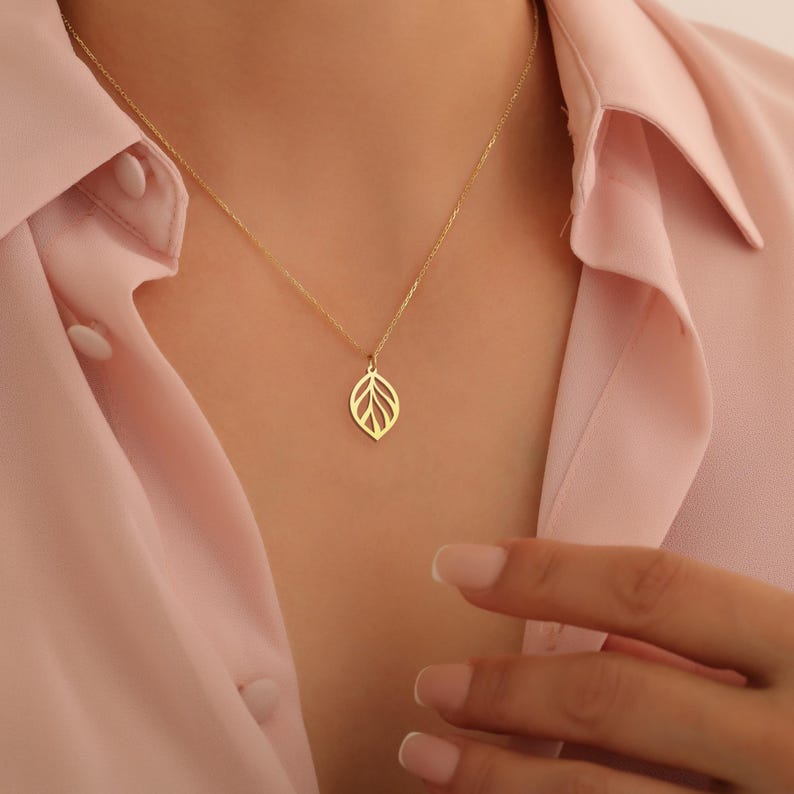 May include: A gold necklace with a delicate leaf pendant. The pendant is made of a thin, intricate design and hangs from a delicate chain.
