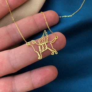 May include: Gold necklace with a pendant of a dog with wings. The dog is outlined in gold and has a delicate design.