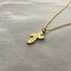 May include: A gold chain necklace with a small, ornate cross pendant. The cross has intricate details and is a traditional design.