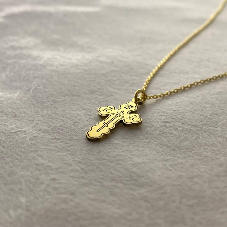 May include: A gold chain necklace with a small, ornate cross pendant. The cross has intricate details and is a traditional design.