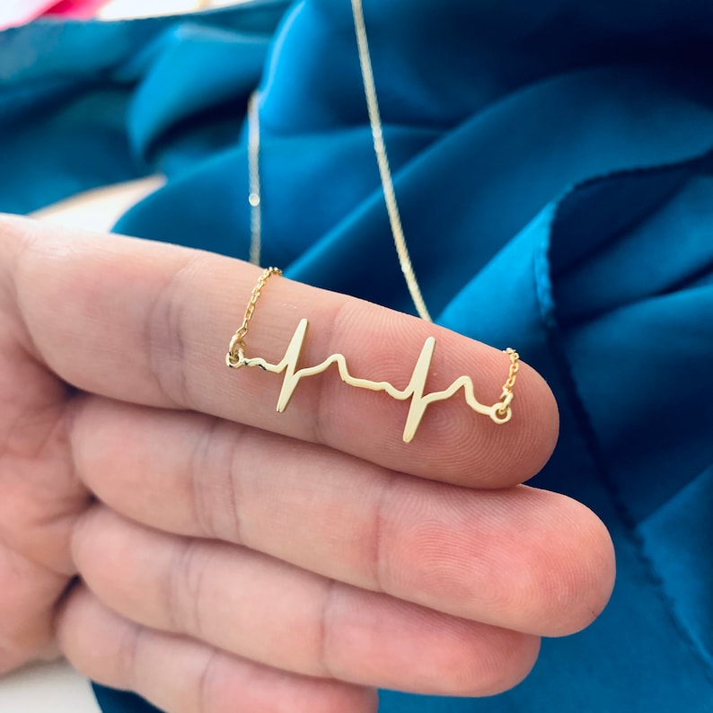 May include: A gold necklace with a heartbeat pendant. The pendant is a simple, stylized design of a heartbeat.