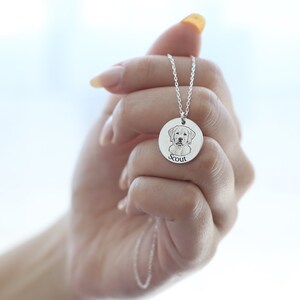 May include: A silver pendant necklace with a detailed engraving of a dog's face. The dog's name, "Scout," is inscribed below the image. The pendant hangs from a delicate silver chain, creating a personalized and sentimental piece of jewellery.