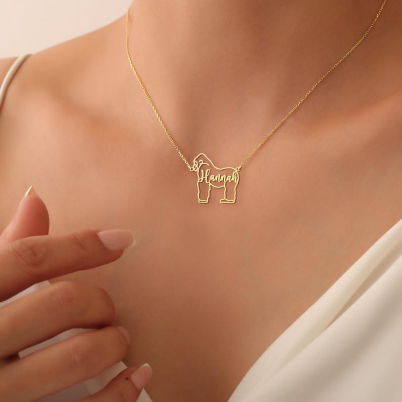 May include: Gold necklace with a gorilla pendant. The gorilla's outline is formed by the name "Hannah".