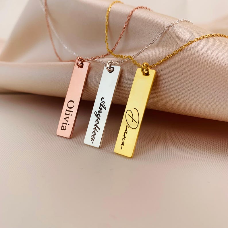 Puede incluir: Tres collares de barra de oro con nombres personalizados grabados en ellos. Los nombres son Olivia, Angelina y Diana.