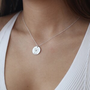 May include: A silver necklace with a circular pendant. The pendant has an engraved illustration of a dog and the name "Scout" below. The pendant hangs from a fine chain, creating a simple and elegant design.