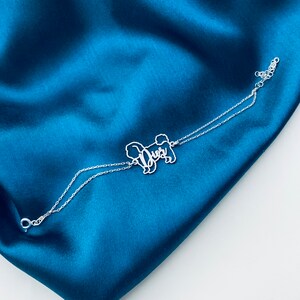 May include: A silver chain bracelet featuring a cutout of a dog and the word "Lucy" against a blue fabric backdrop.
