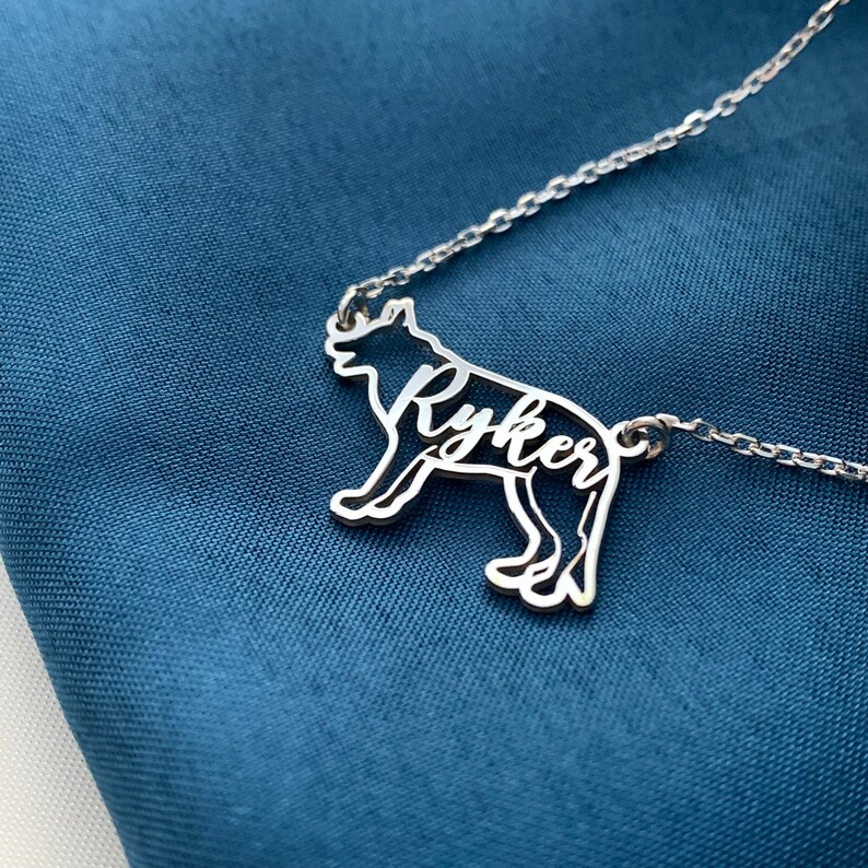 K&ouml;nnte beinhalten: Silberne Halskette mit einem Wolf-Silhouetten-Anh&auml;nger. Der Name "Ryker" ist aus dem K&ouml;rper des Wolfes ausgeschnitten.