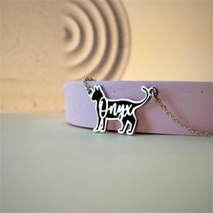 May include: A silver necklace with a black cat charm. The cat's silhouette is outlined in silver, and the word "Onyx" is written inside the cat's body.