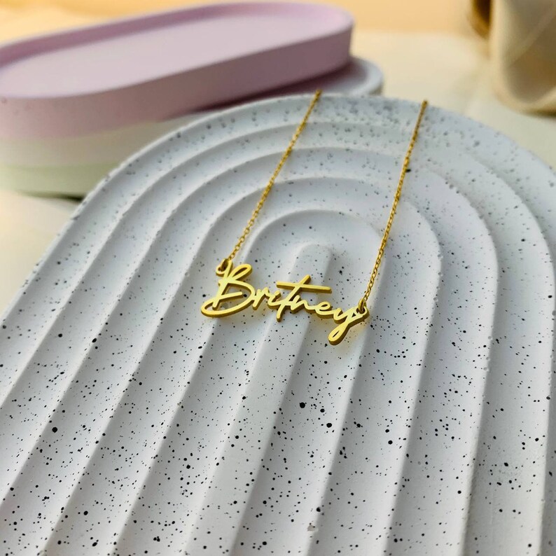 May include: A gold necklace with the name "Britney" written in a cursive script.
