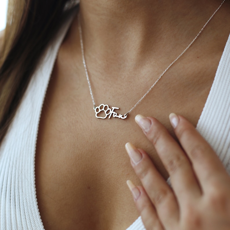May include: Silver necklace with a paw print charm and the word "Fave" spelled out.
