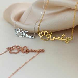 May include: Three silver, gold, and rose gold necklaces with a paw print charm and a personalized name. The names are "Fox", "Lucky", and "Oscar".