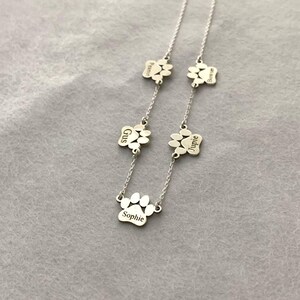 May include: Silver necklace with five paw print charms, each engraved with a different name: Sophie, Gus, Jupie, Bonnie, and Peanut.
