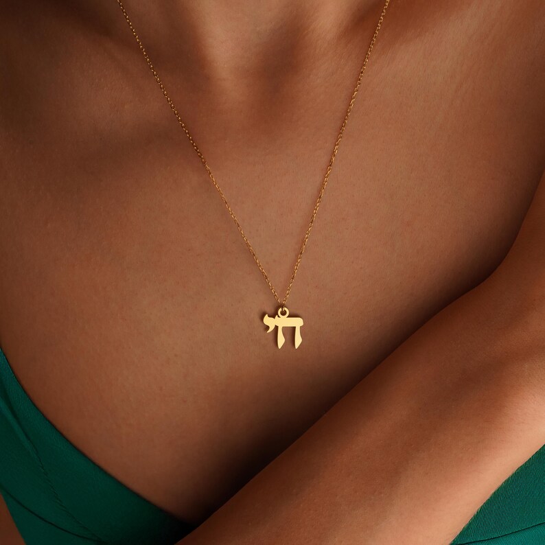 Peut inclure: Un collier dor&eacute; avec un pendentif en forme de la lettre h&eacute;bra&iuml;que &laquo;&nbsp;Chai&nbsp;&raquo;, signifiant &laquo;&nbsp;vie&nbsp;&raquo;. Le pendentif est suspendu &agrave; une fine cha&icirc;ne. Le collier est pr&eacute;sent&eacute; sur une personne portant un haut vert.