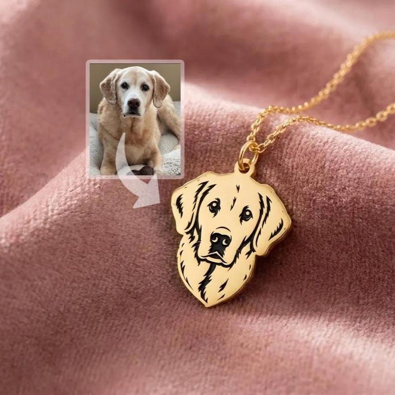 May include: A gold-colored pendant necklace featuring a dog's head silhouette. The pendant is a detailed outline of a dog's face. The necklace is on a pink surface, with a small image of a dog in the upper left corner.