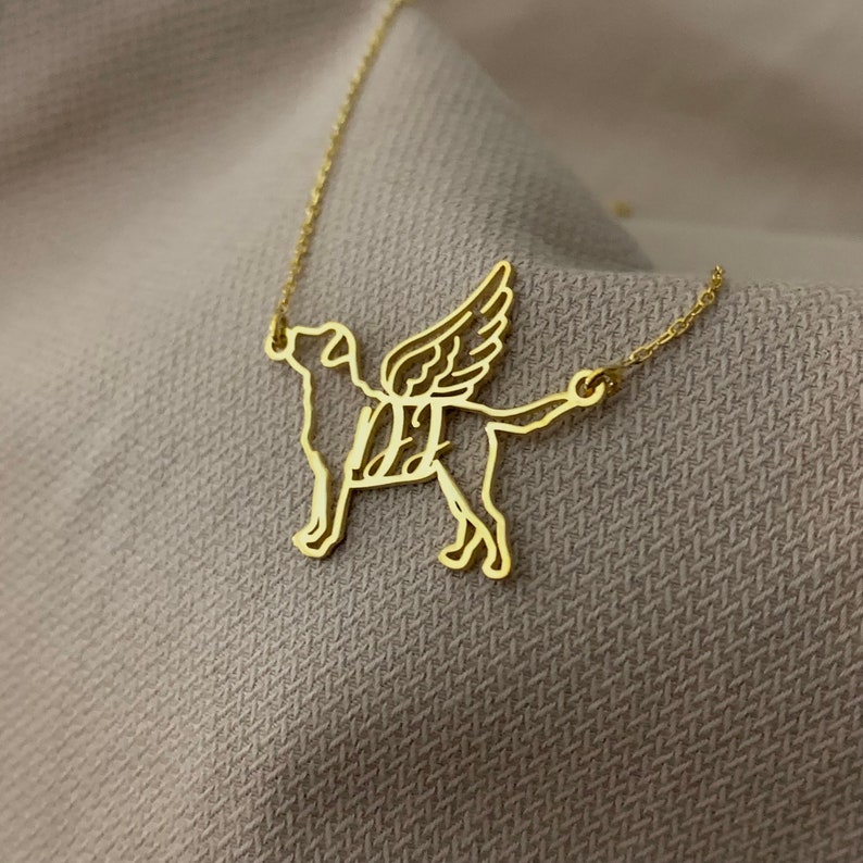 Puede incluir: Collar de oro con un recorte detallado de un perro con alas. El perro est&aacute; mirando hacia adelante con la cabeza inclinada hacia arriba. Las alas est&aacute;n extendidas detr&aacute;s del perro.