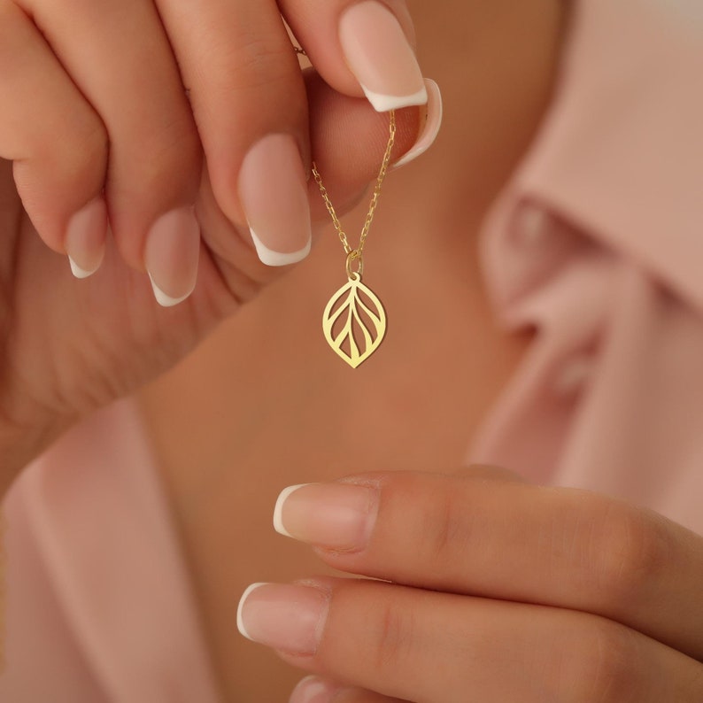 May include: A gold necklace with a delicate leaf pendant. The pendant is made of a thin, openwork design and has a subtle shine.