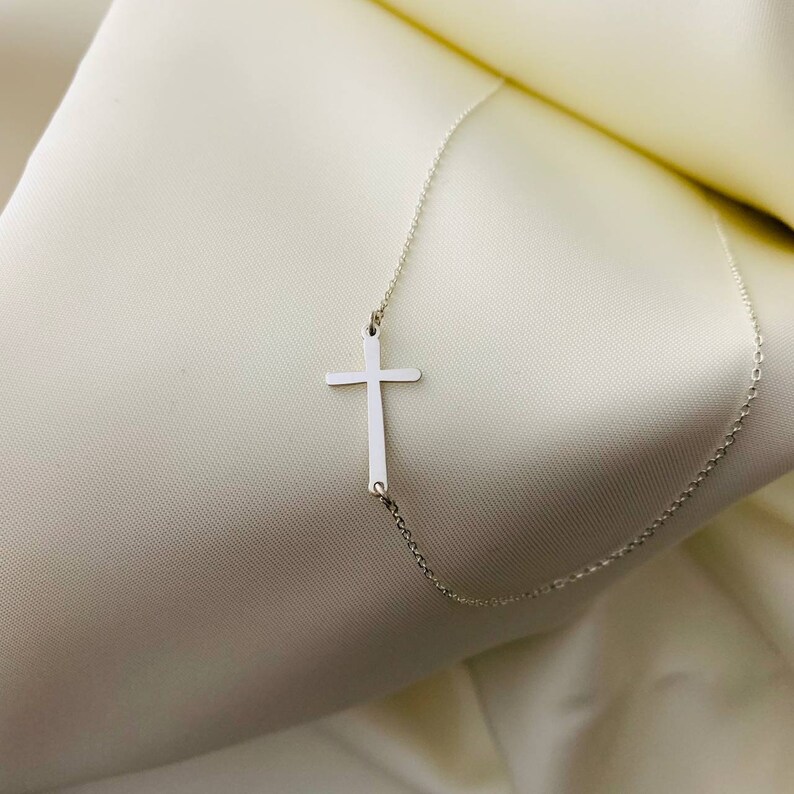 May include: A silver chain necklace with a simple silver cross pendant.