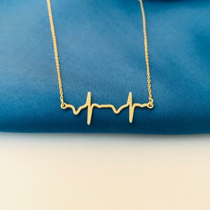 May include: A gold necklace with a delicate heartbeat pendant. The pendant is a simple, minimalist design, perfect for a subtle statement.