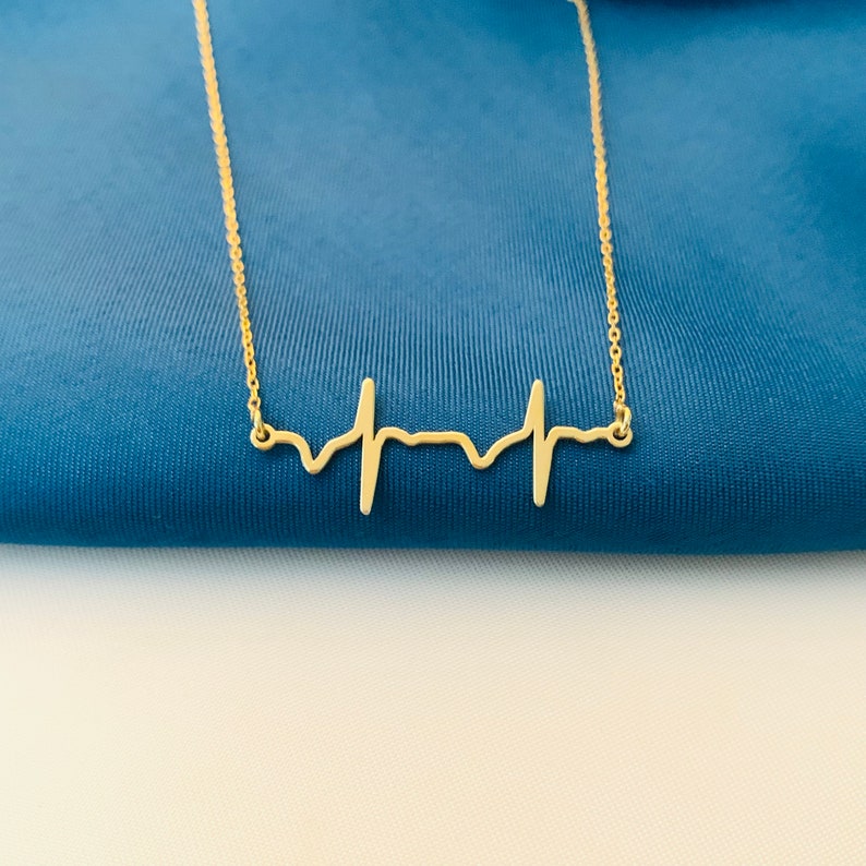 May include: A gold necklace with a delicate heartbeat pendant. The pendant is a simple, minimalist design, perfect for a subtle statement.