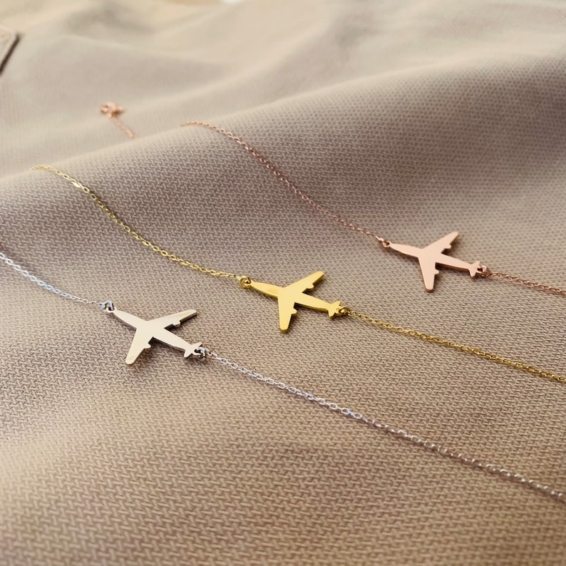 Op de afbeelding: Drie delicate kettingen met vliegtuig hangers. De kettingen zijn zilver, goud en ros&eacute;goud.