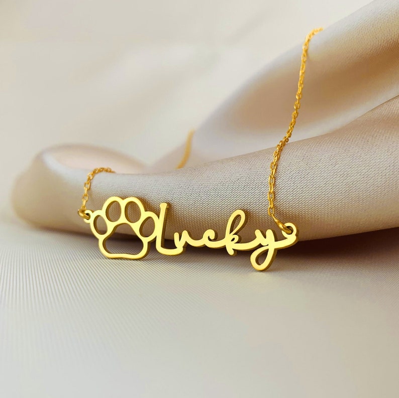 May include: Gold necklace with a paw print charm and the word "Lucky" written in cursive.
