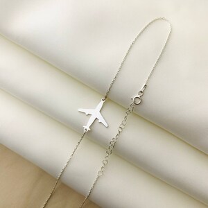 Op de afbeelding: Een zilveren ketting met een vliegtuighanger. De ketting is delicaat en het vliegtuig is een eenvoudige silhouet.