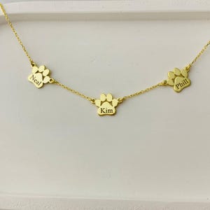 May include: Gold necklace with three paw print charms, each engraved with a name: Neal, Kim, and Phill.