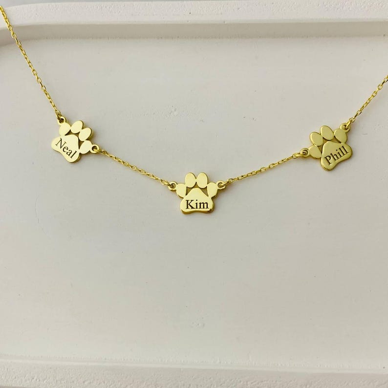 May include: Gold necklace with three paw print charms, each engraved with a name: Neal, Kim, and Phill.
