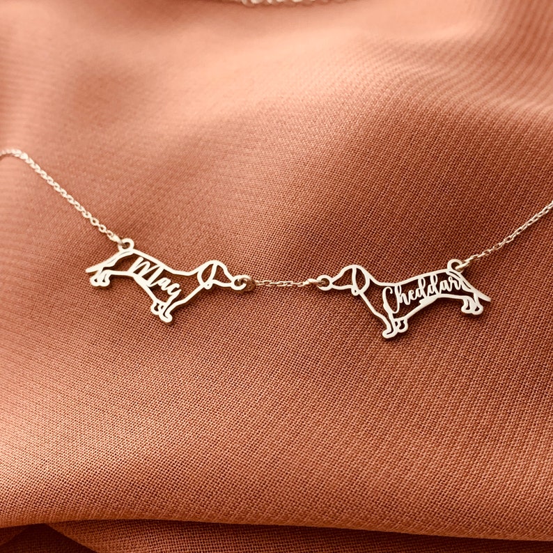 May include: Silver dachshund silhouette necklace with the names "Max" and "Cheddar" inscribed on each dachshund.