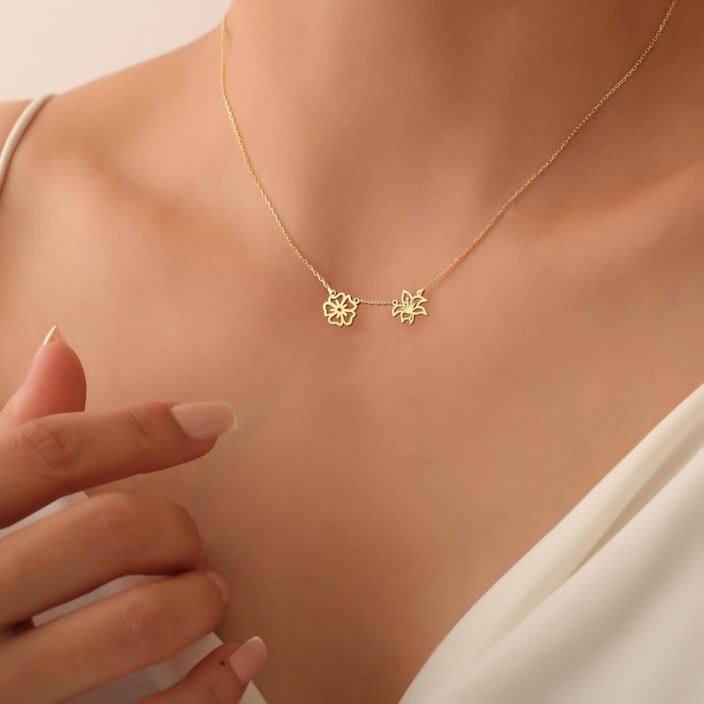 K&ouml;nnte beinhalten: Eine zarte goldene Halskette mit zwei bl&uuml;tenf&ouml;rmigen Anh&auml;ngern. Die Kette wird von einem Model getragen.