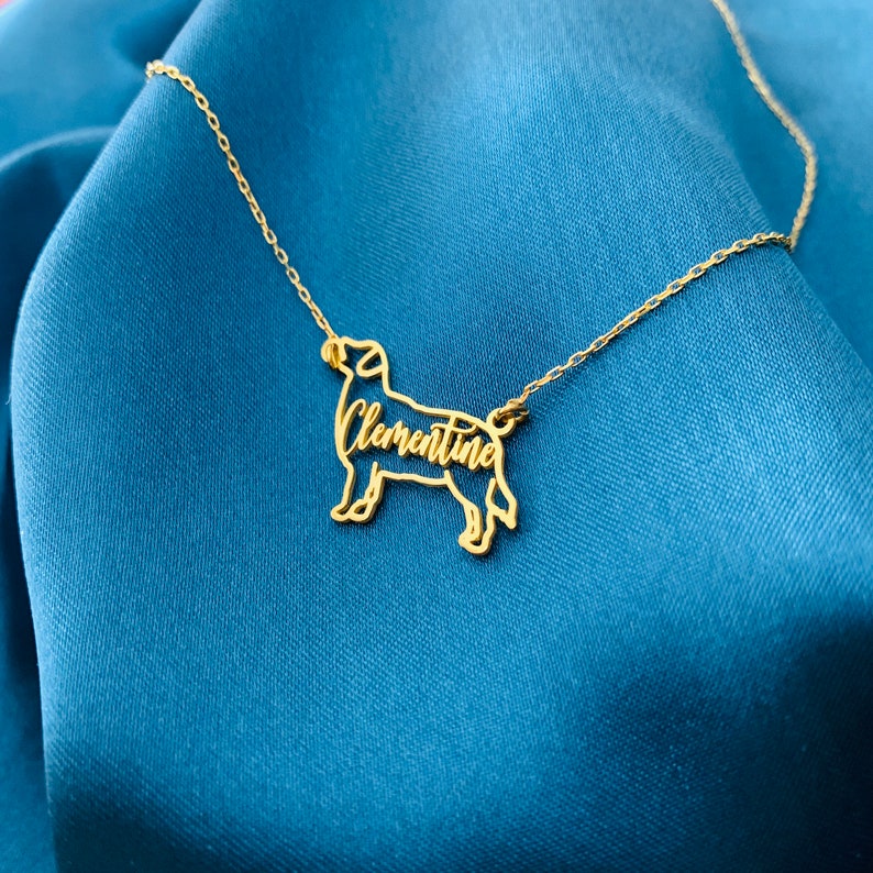 May include: Gold necklace with a dog silhouette pendant. The dog's name, "Clementine", is cut out of the pendant.