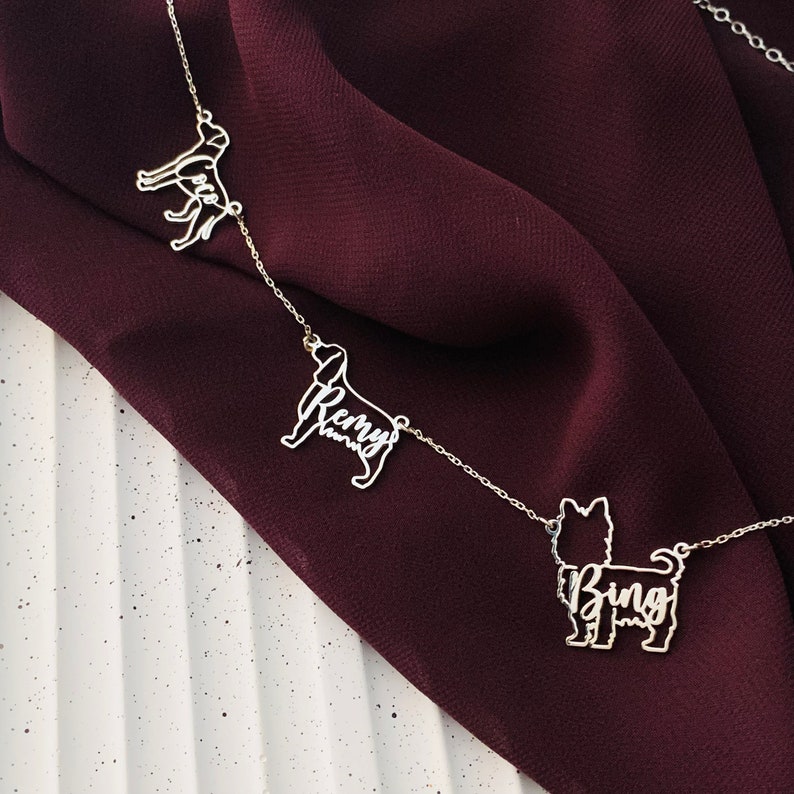 May include: A silver necklace with three dog silhouette charms. The charms are engraved with the names "Bing", "Remy", and "Luca".