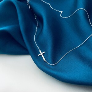 May include: A silver cross pendant necklace on a blue satin background.