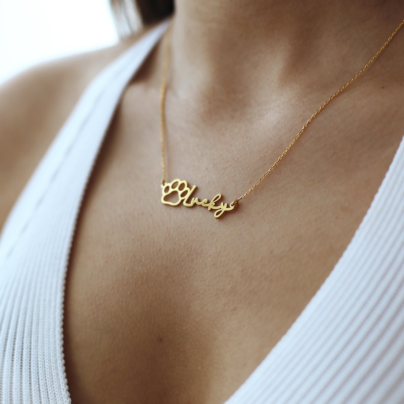 May include: Gold necklace with a paw print charm and the name "Lucky" written in cursive.