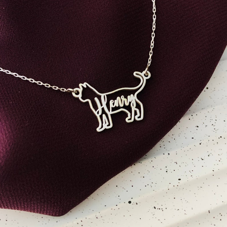 May include: Silver necklace featuring a cat silhouette pendant. The cat's outline is filled with the name "Henry" in cursive.