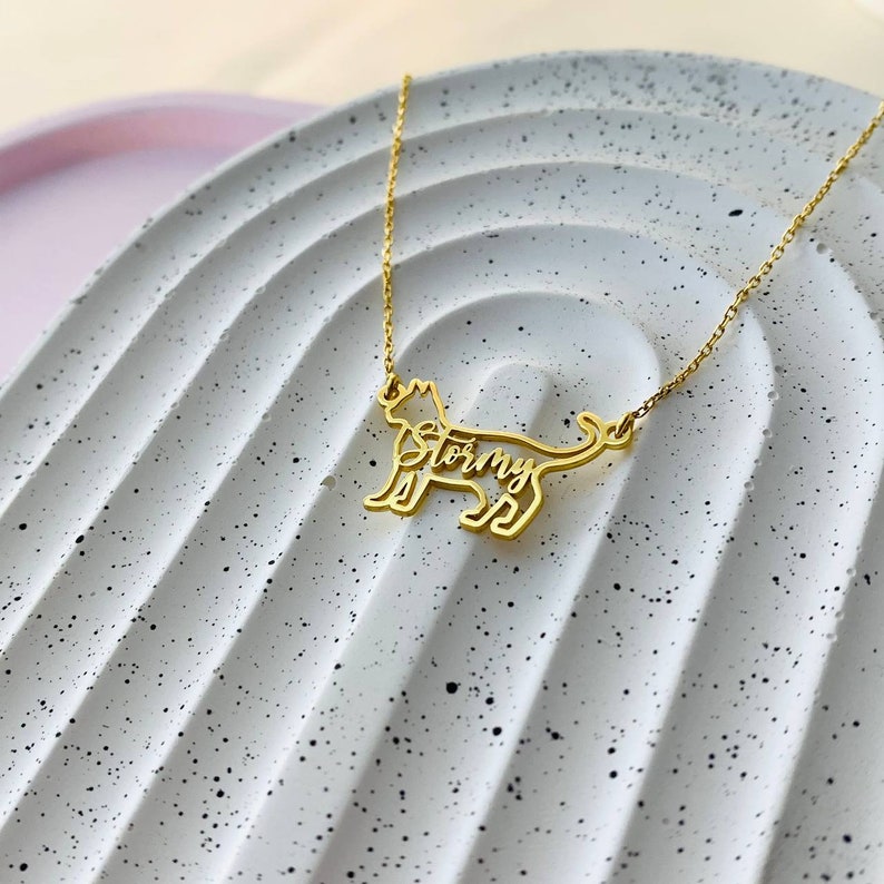 May include: Gold necklace featuring a cat-shaped pendant. The cat's silhouette is cut out with the name "Stormy" inscribed within the outline.